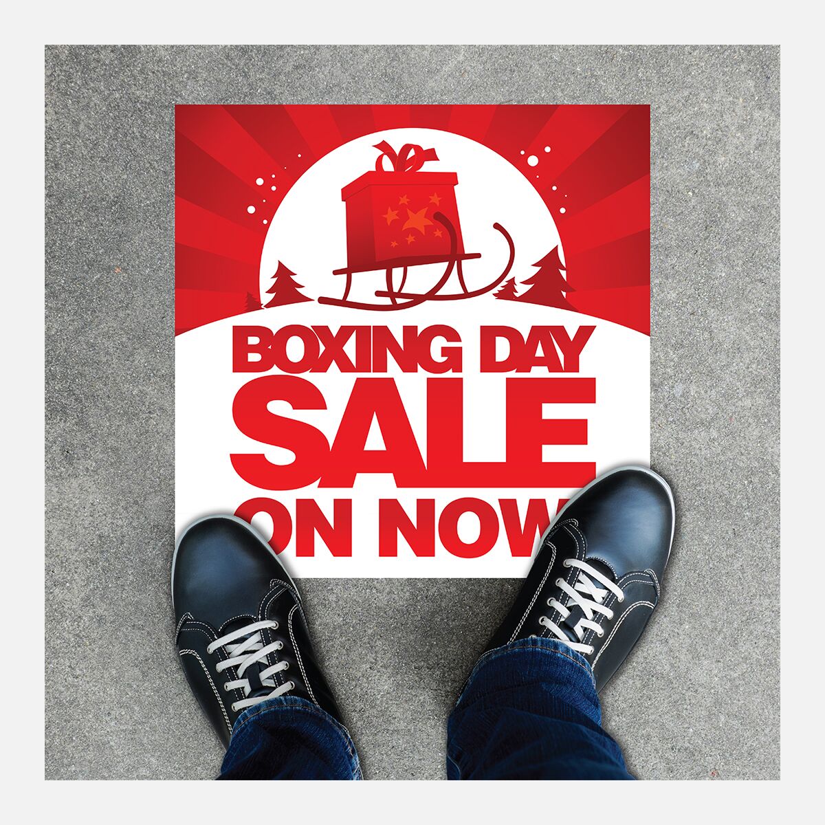 Square outdoor floor decal reading “Boxing Day sale on now” on pavement beside a person’s shoes